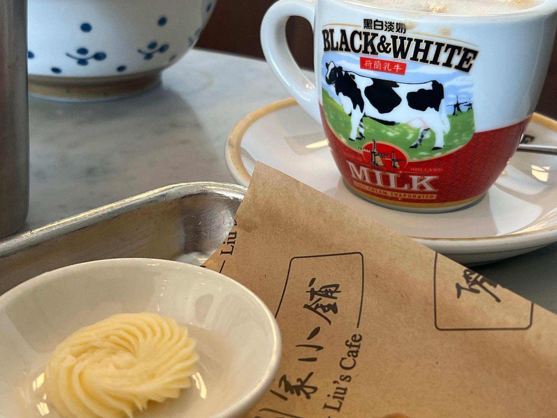 Cup with Black & White milk logo beside a small dish of butter on a café table.