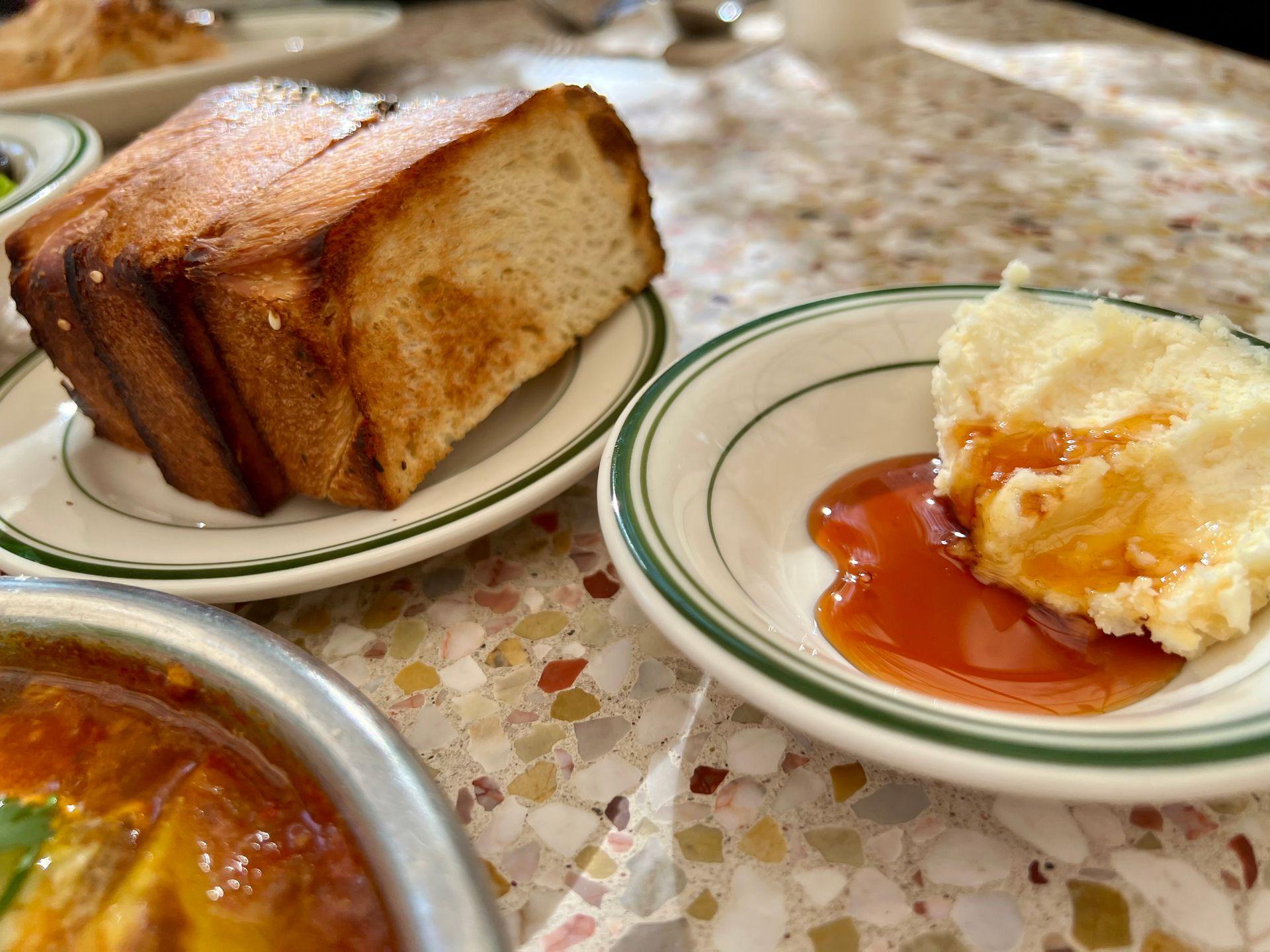 Slices of toasted bread on a plate next to a small dish of cheesecake topped with caramel sauce.