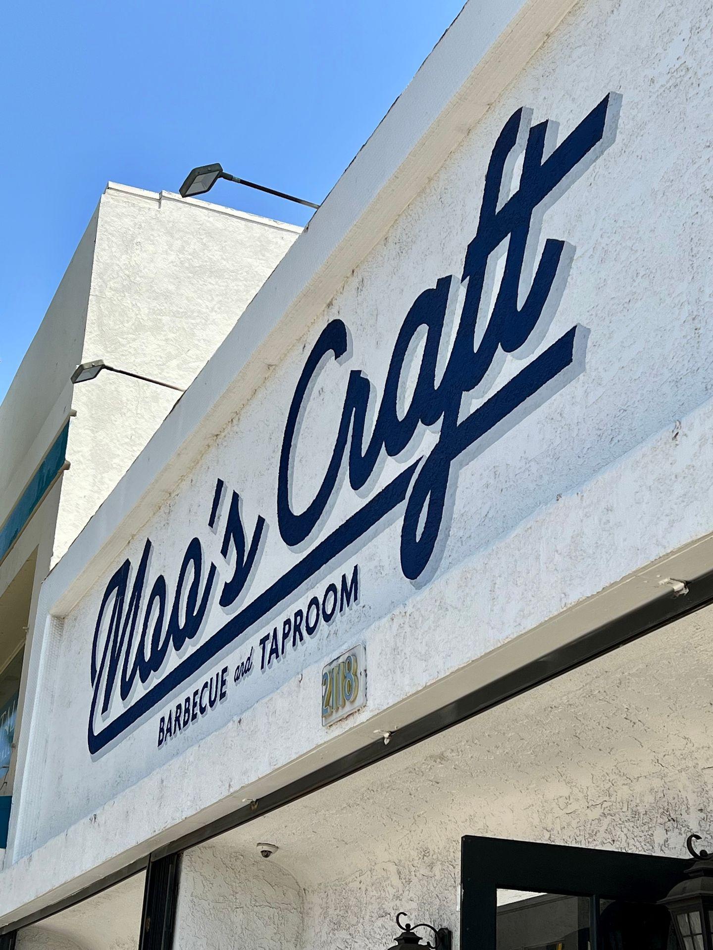 Sign of a barbecue and taproom with bold blue lettering against a white wall.