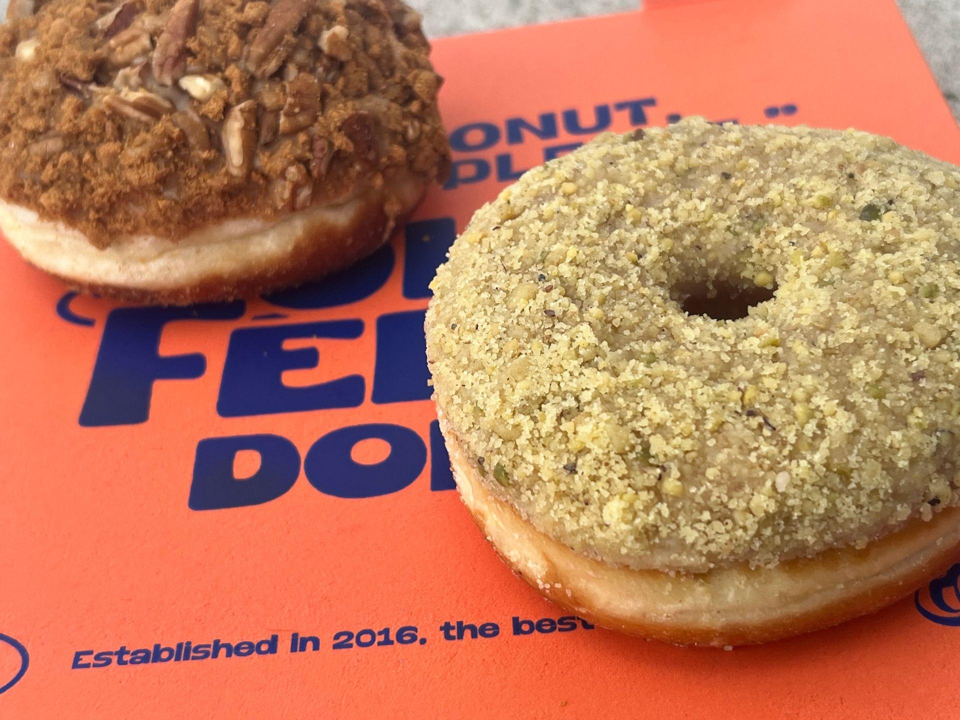 Two gourmet donuts with crumb toppings on an orange box with text.