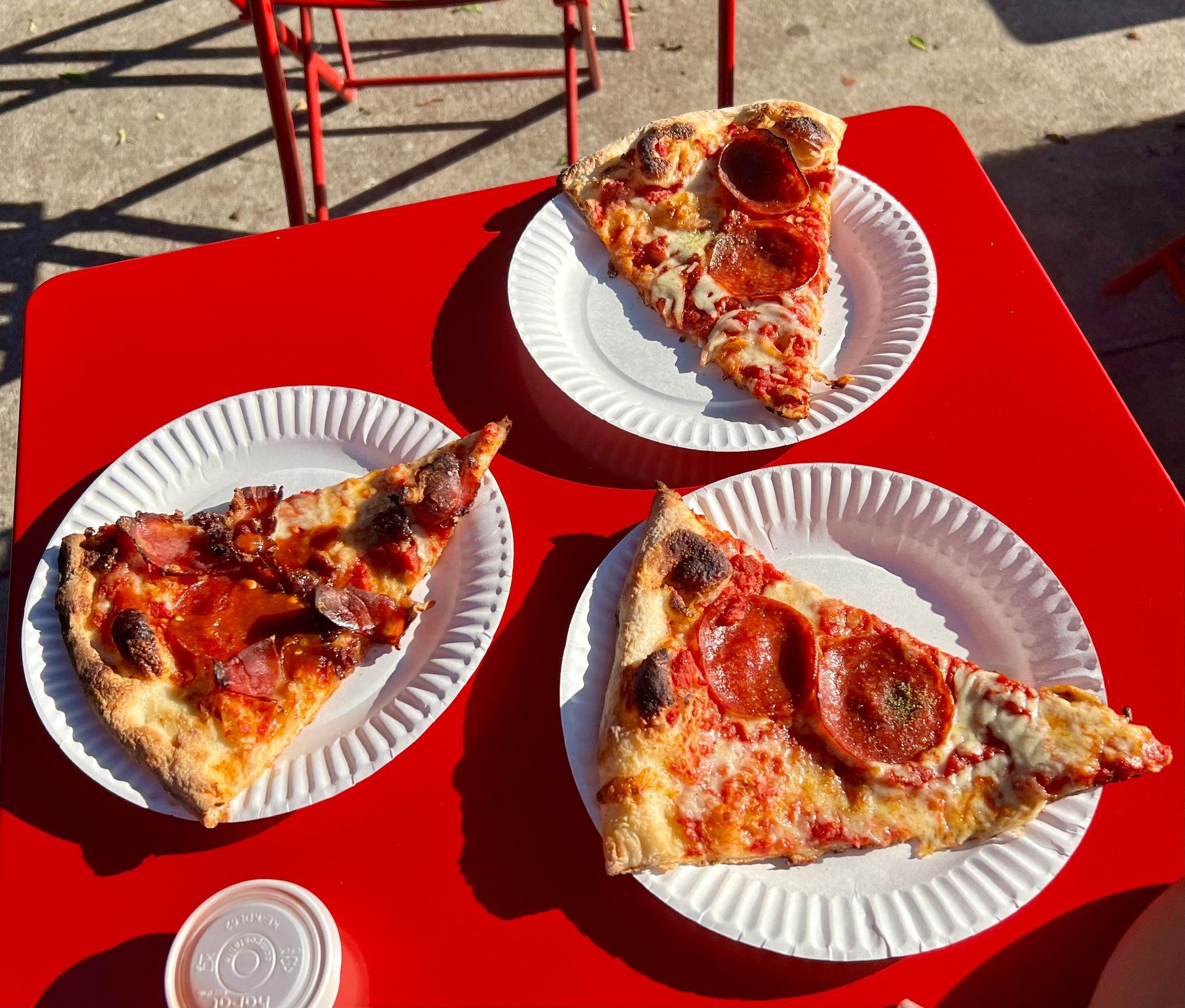 Three slices of pepperoni pizza on paper plates placed on a red table.