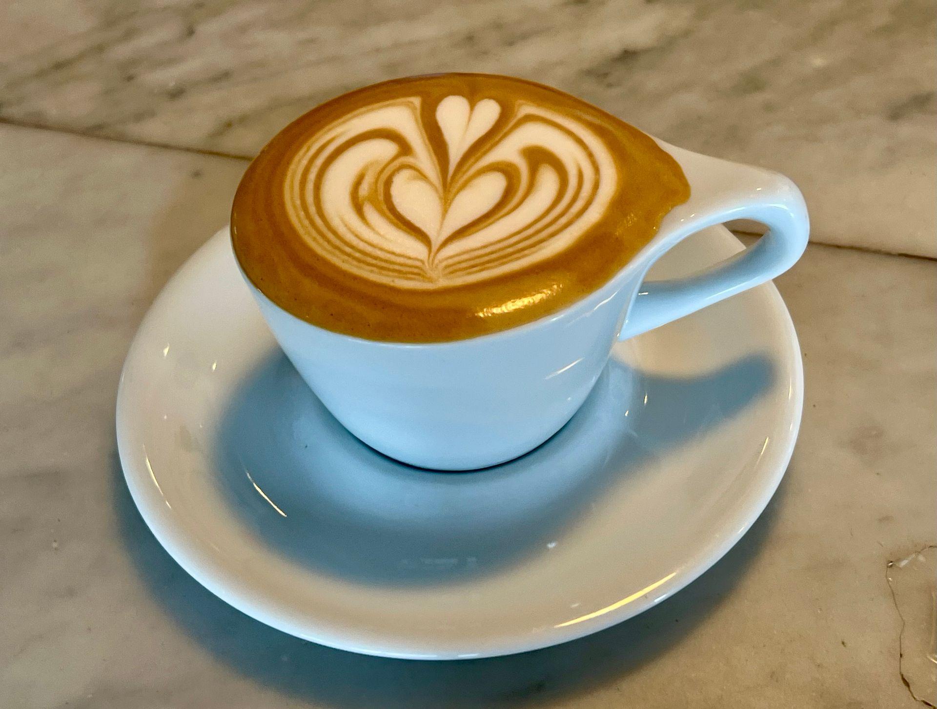 Cup of latte with heart-shaped latte art on a marble table.