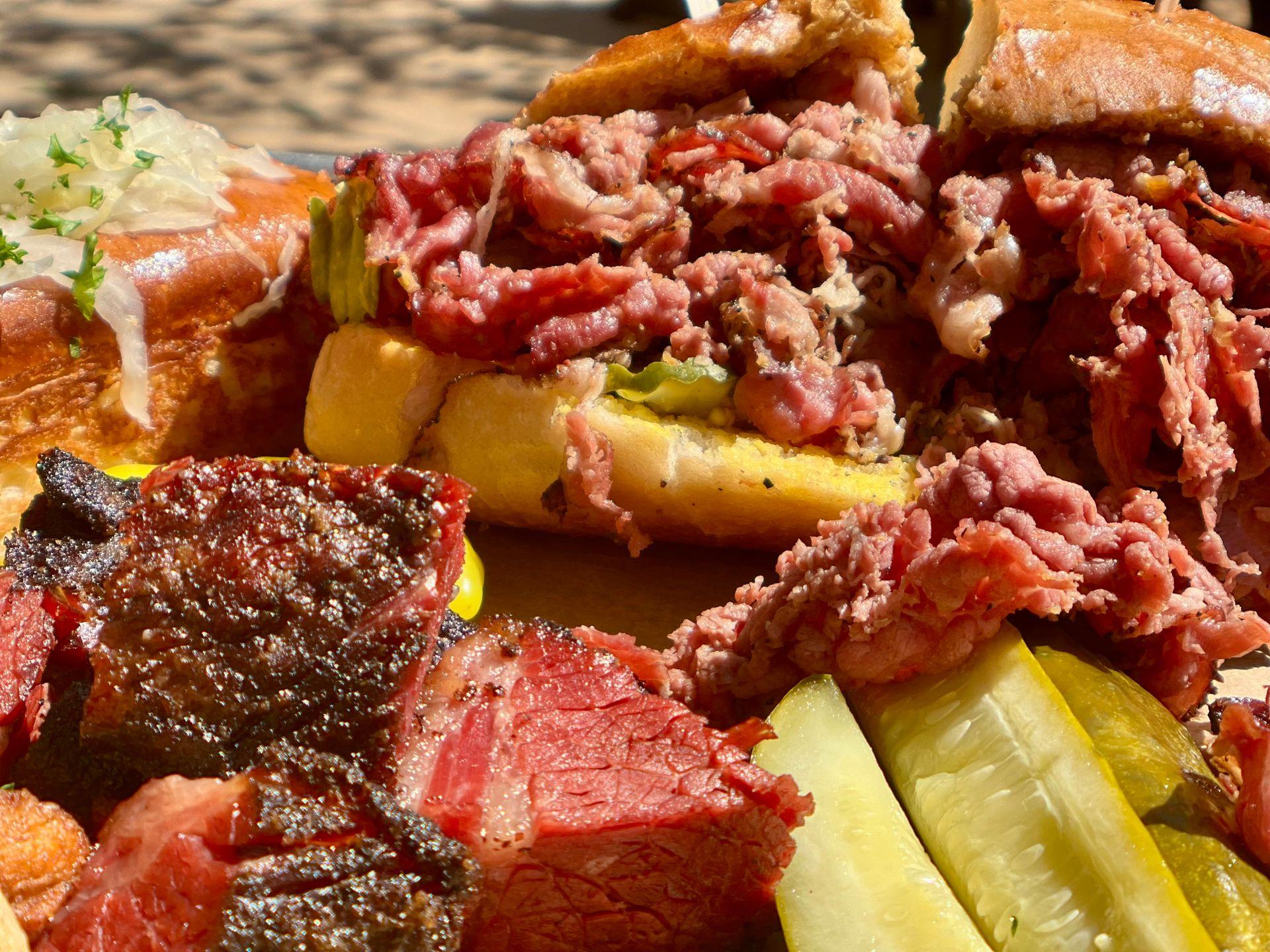 Close-up of a sandwich filled with sliced roast beef, pickles, and grilled meat.