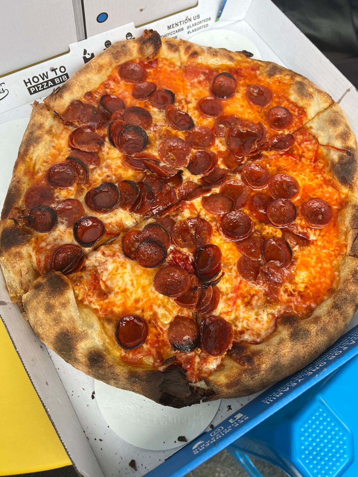 Close-up of a pepperoni pizza with a crispy crust in an open cardboard box.