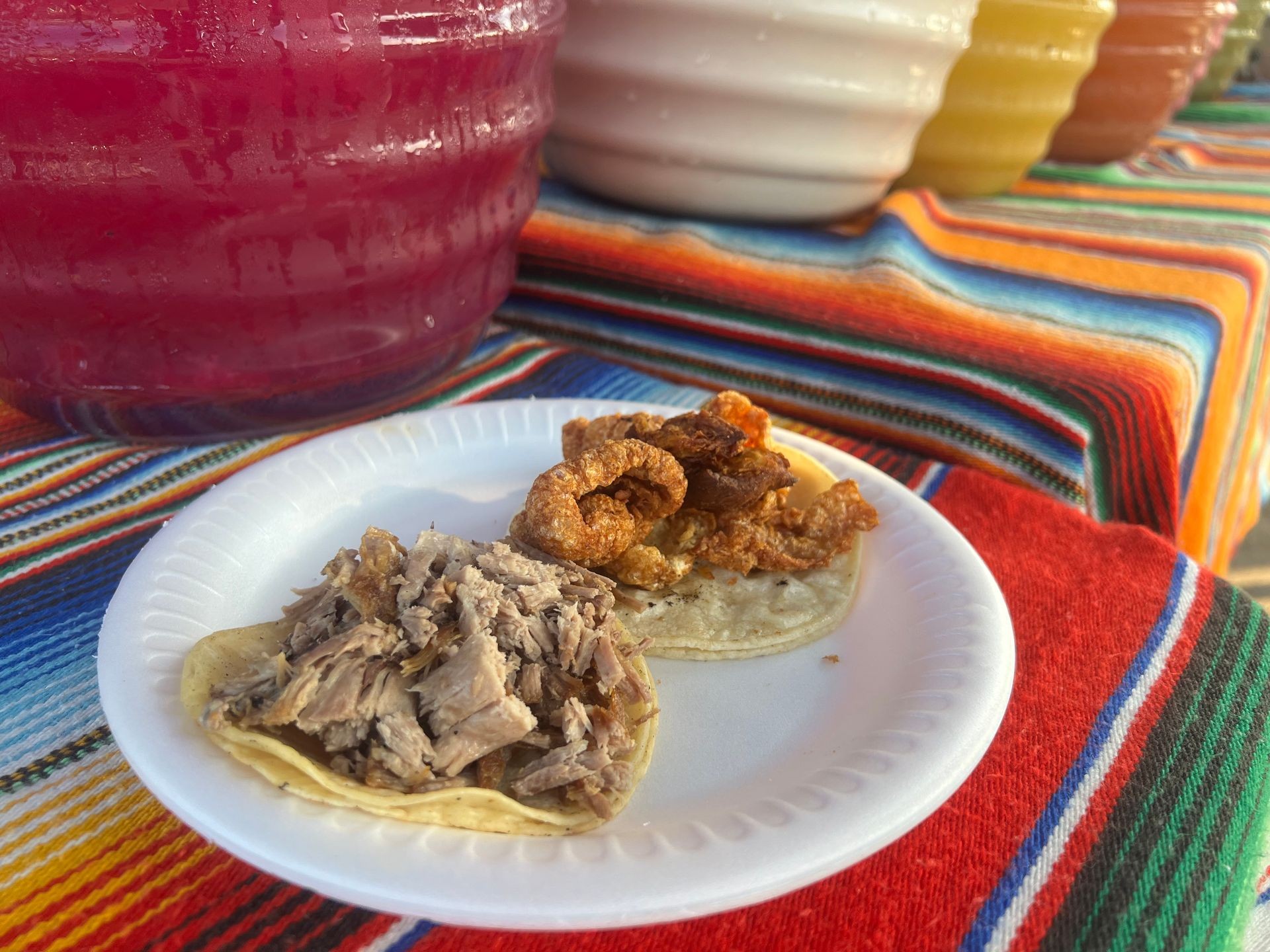 Tacos and vibrant drink on colorful tablecloth.