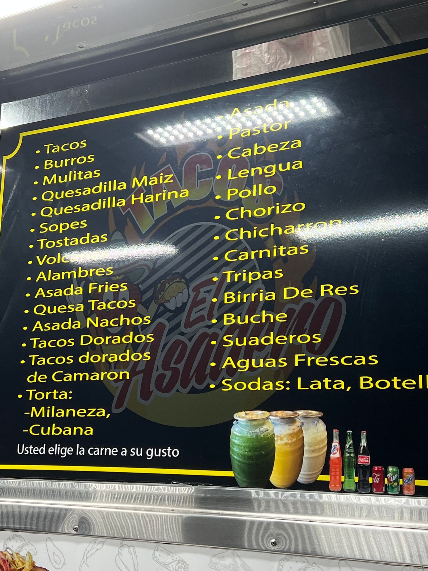 Menu board with Mexican food items and drinks options in yellow text, accompanied by images of beverages.