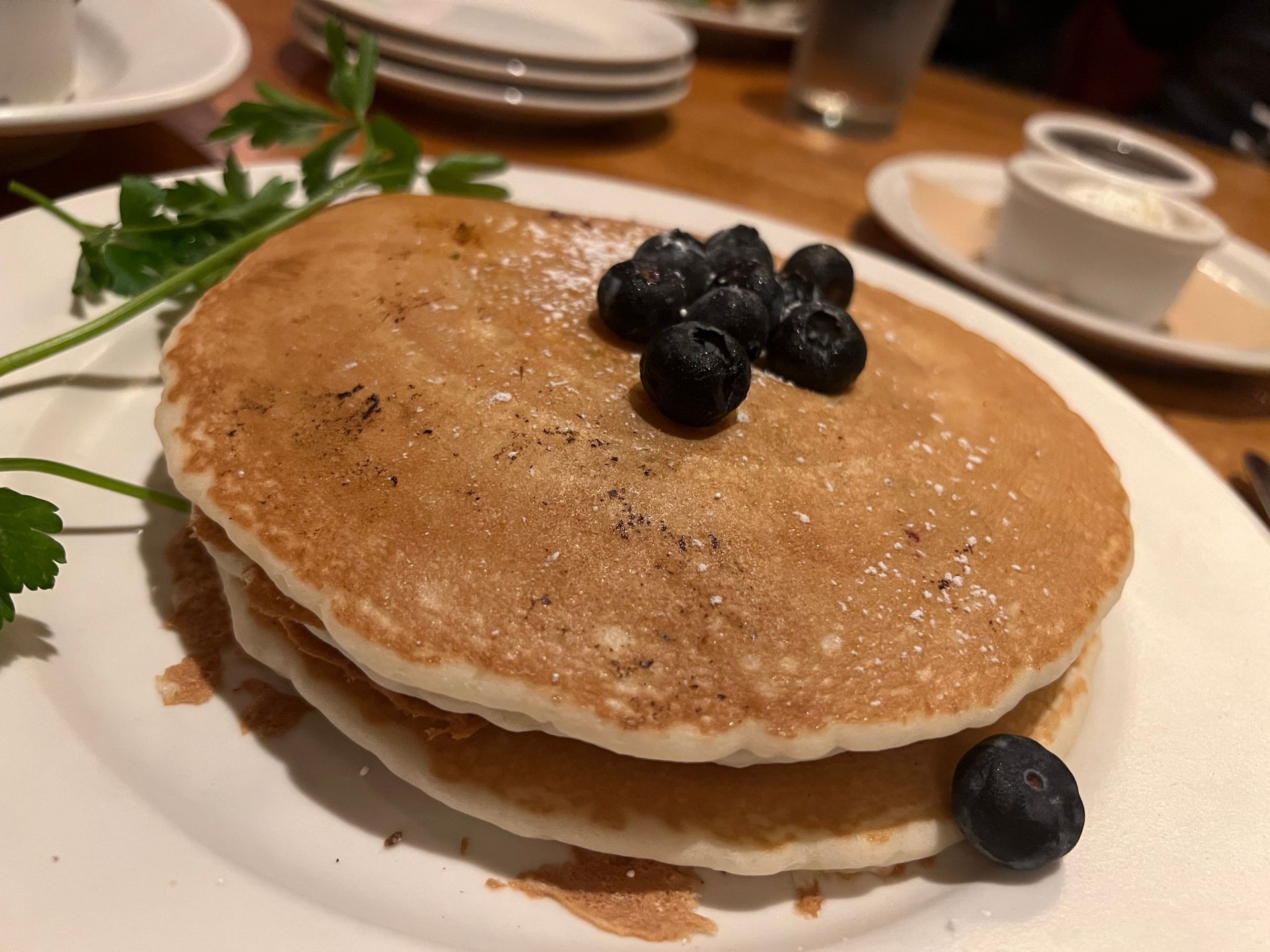 Stack of pancakes topped with blueberries on a white plate, garnished with parsley.