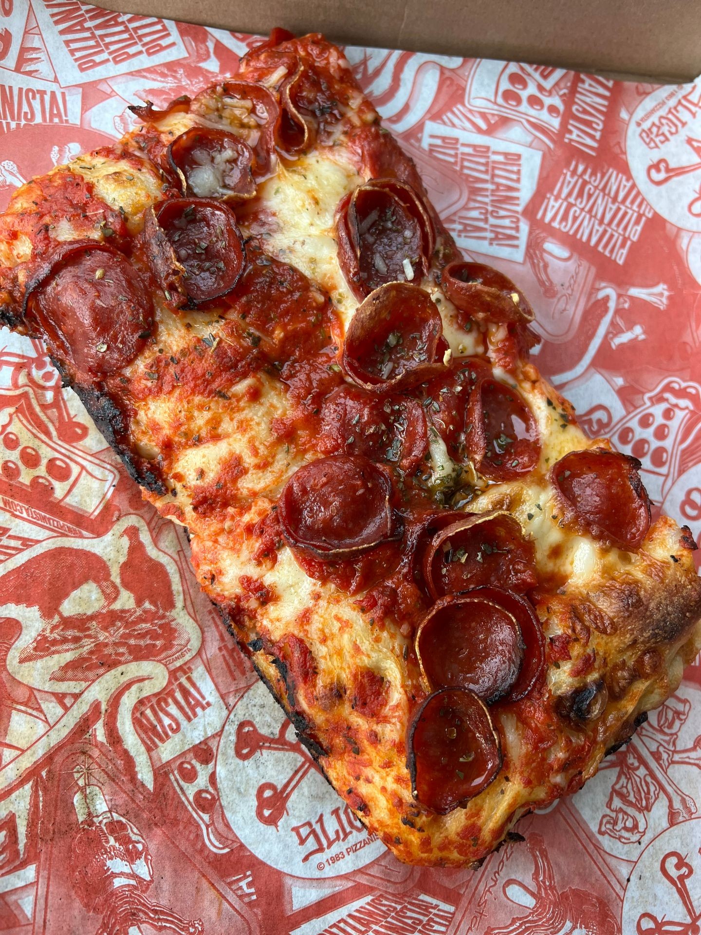 Close-up of a rectangular pepperoni pizza slice on red and white patterned paper.