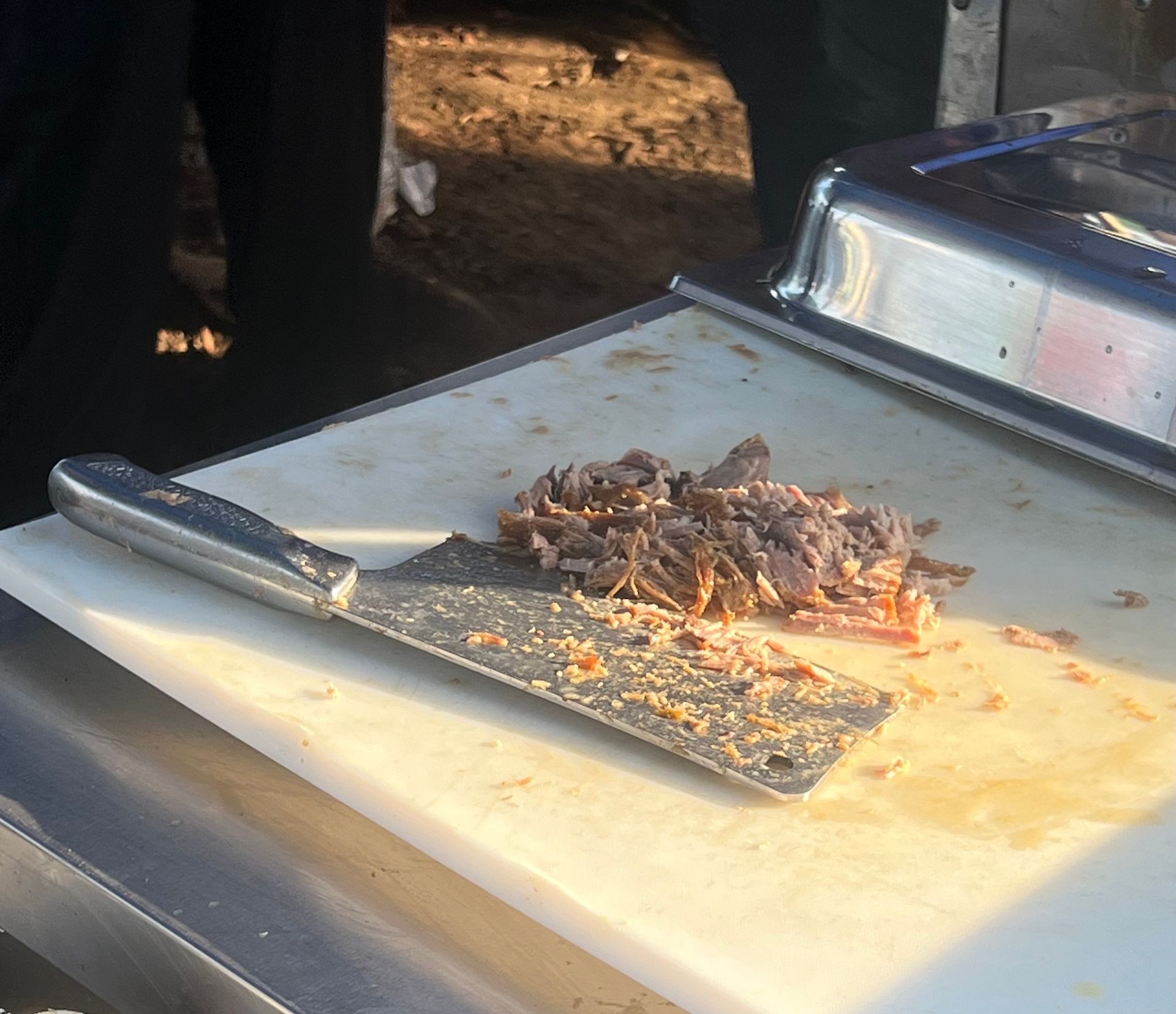 Chopped meat on a cutting board with a large knife under the sunlight.