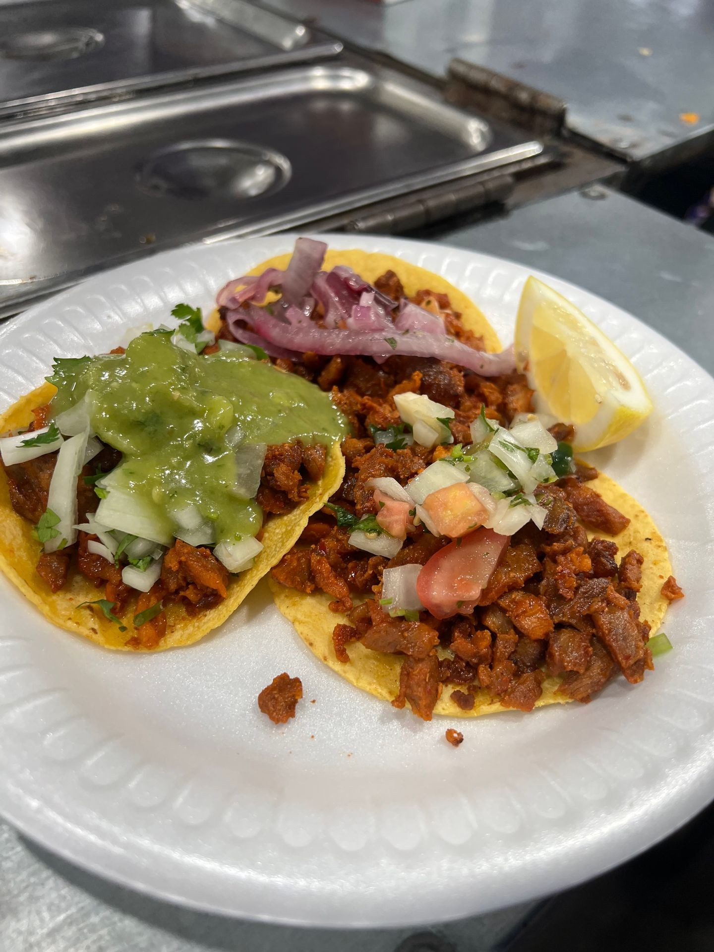 Two tacos topped with meat, salsa, onions, and a lemon wedge on a white plate.